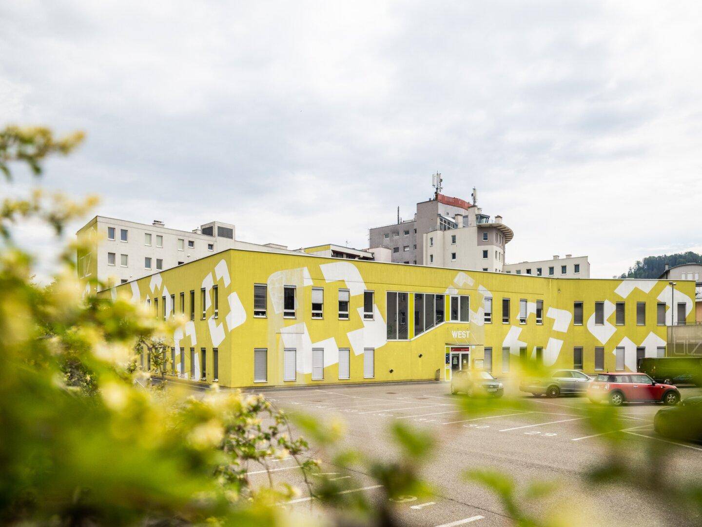 Modernes Gebäude mit auffälliger gelber Fassade und weißen geometrischen Mustern, umgeben von Parkplätzen.