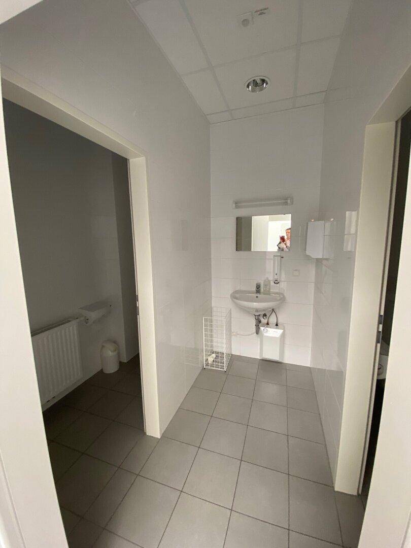 Sauberer Toilettenbereich mit grauen Bodenfliesen, weißen Wandfliesen, Waschbecken und Spiegel, in gutem Zustand.