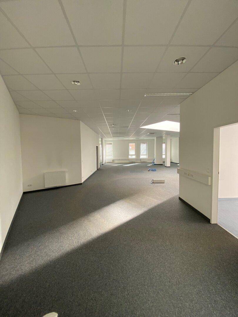 Langer, offener Bürobereich mit Teppichboden und einem Oberlicht in der Ferne, das den Raum erhellt.
