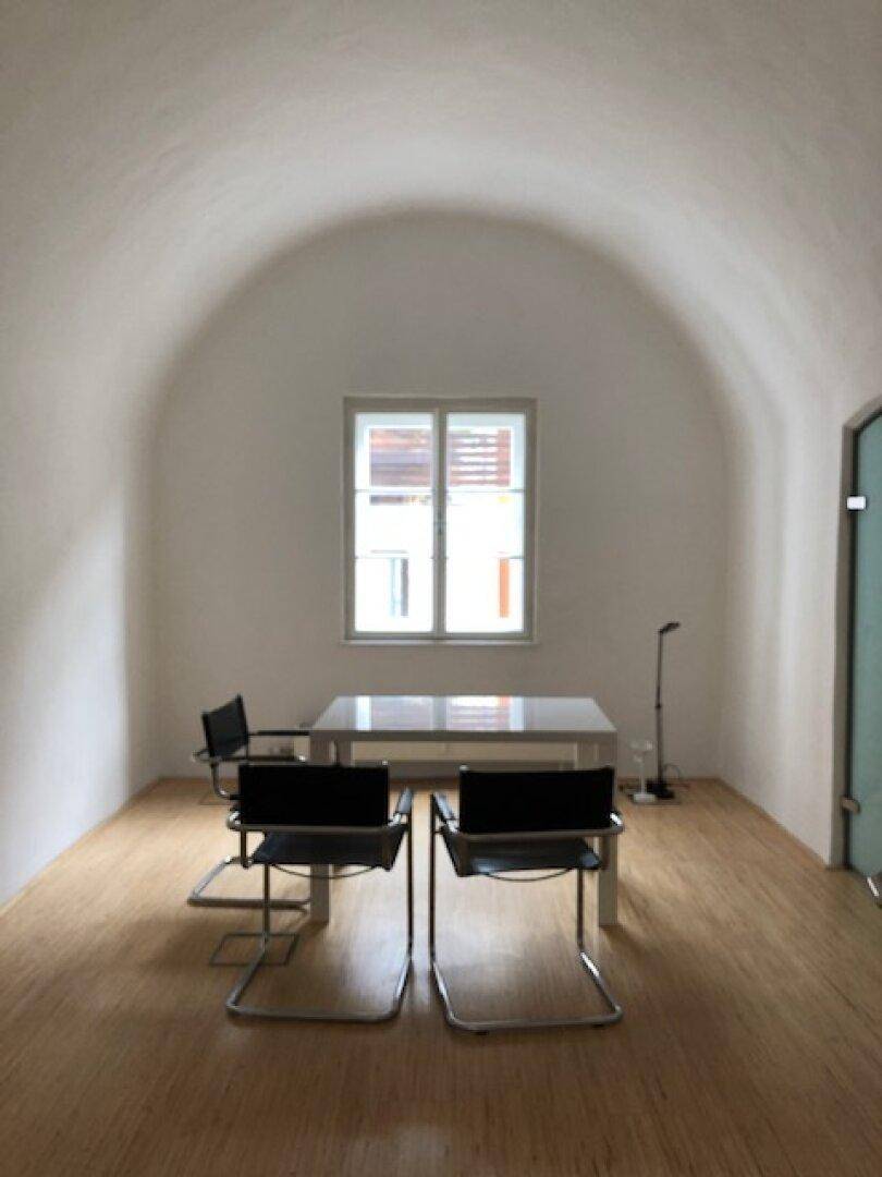 Heller Büroraum mit beeindruckender Gewölbedecke, Holzboden und einem Fenster mit Blick nach draußen.