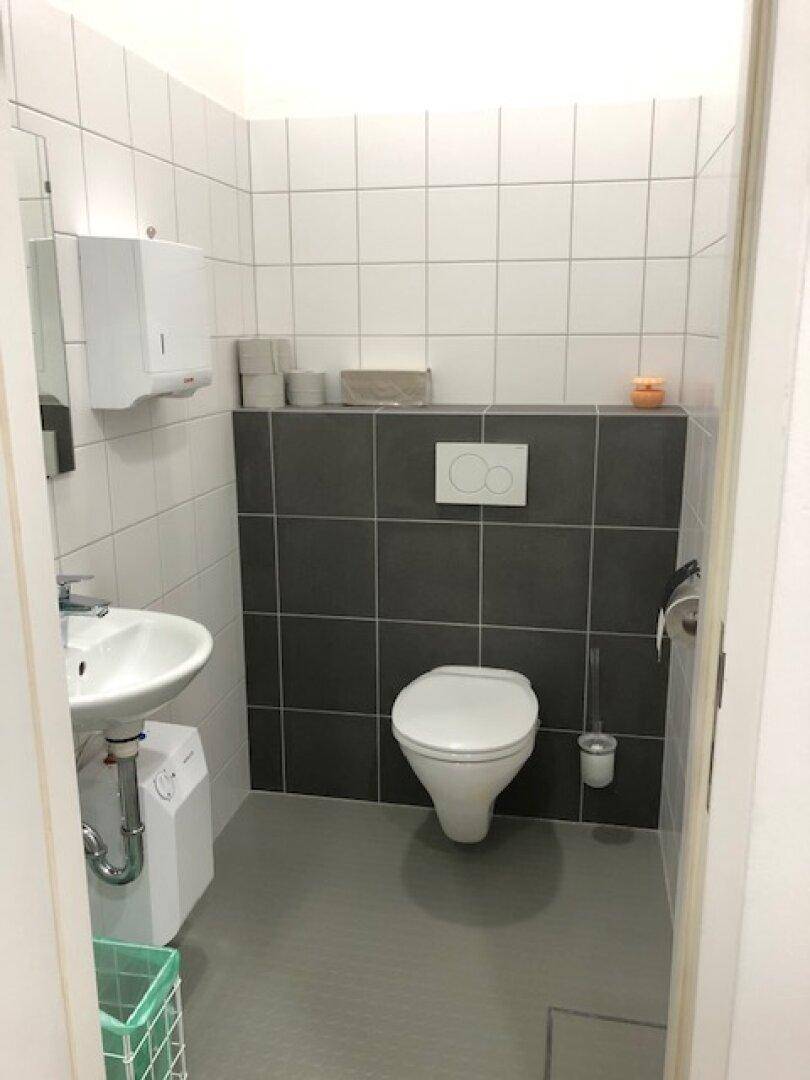 Modern gefliestes Gäste-WC mit weißer Toilette, kleinem Waschbecken und grauen Akzentfliesen.