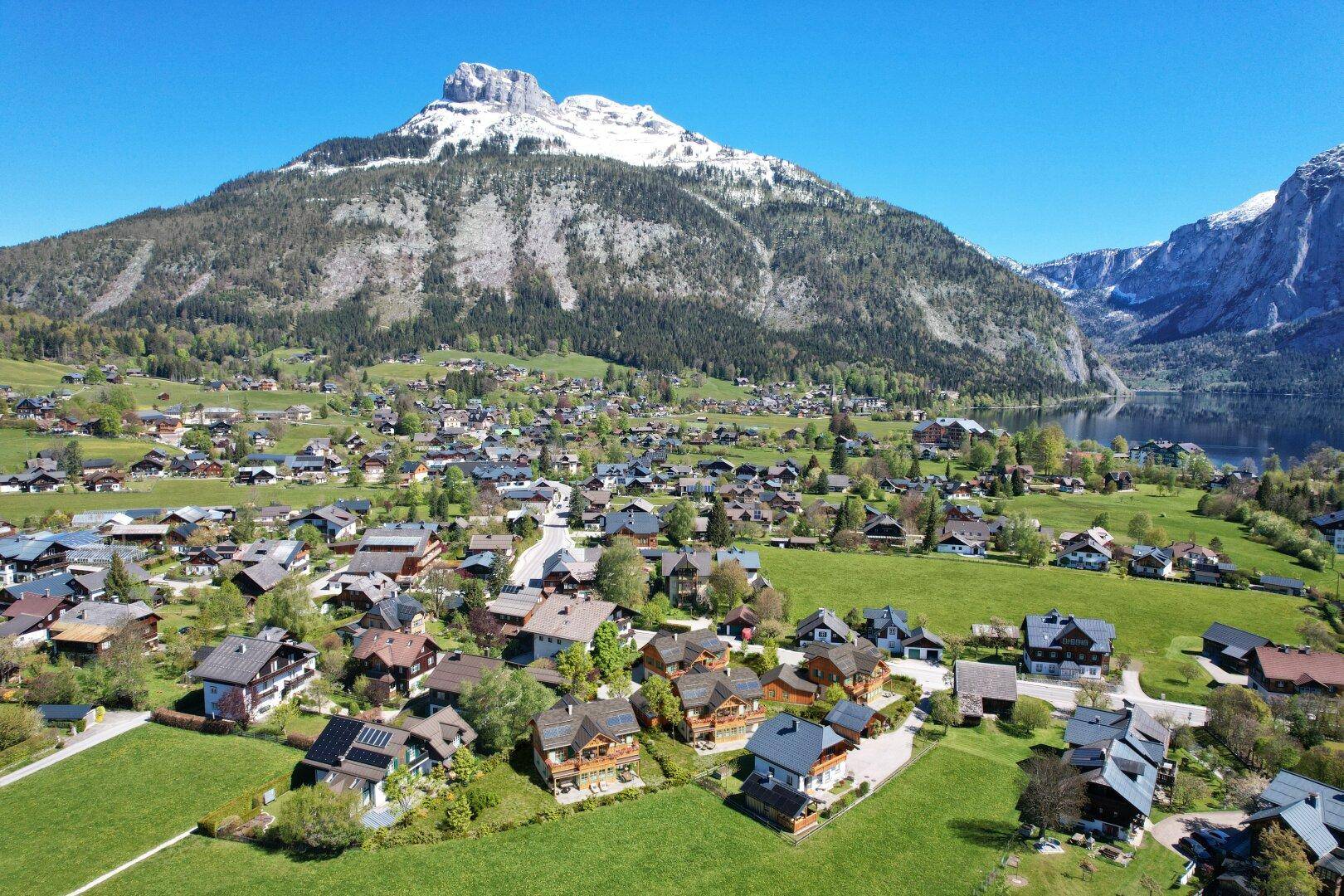 Luftaufnahme eines malerischen Dorfes mit See- und Bergblick in einer weiten alpinen Landschaft.