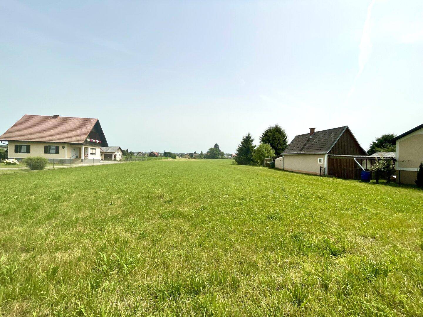 Weitläufige grüne Landschaft mit einzelnen Wohnhäusern unter klarem Himmel.