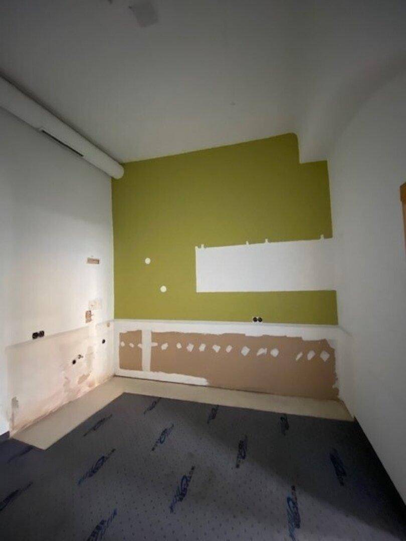 Kleiner Raum in Renovierung mit grüner Akzentwand und vorbereiteten Installationen.