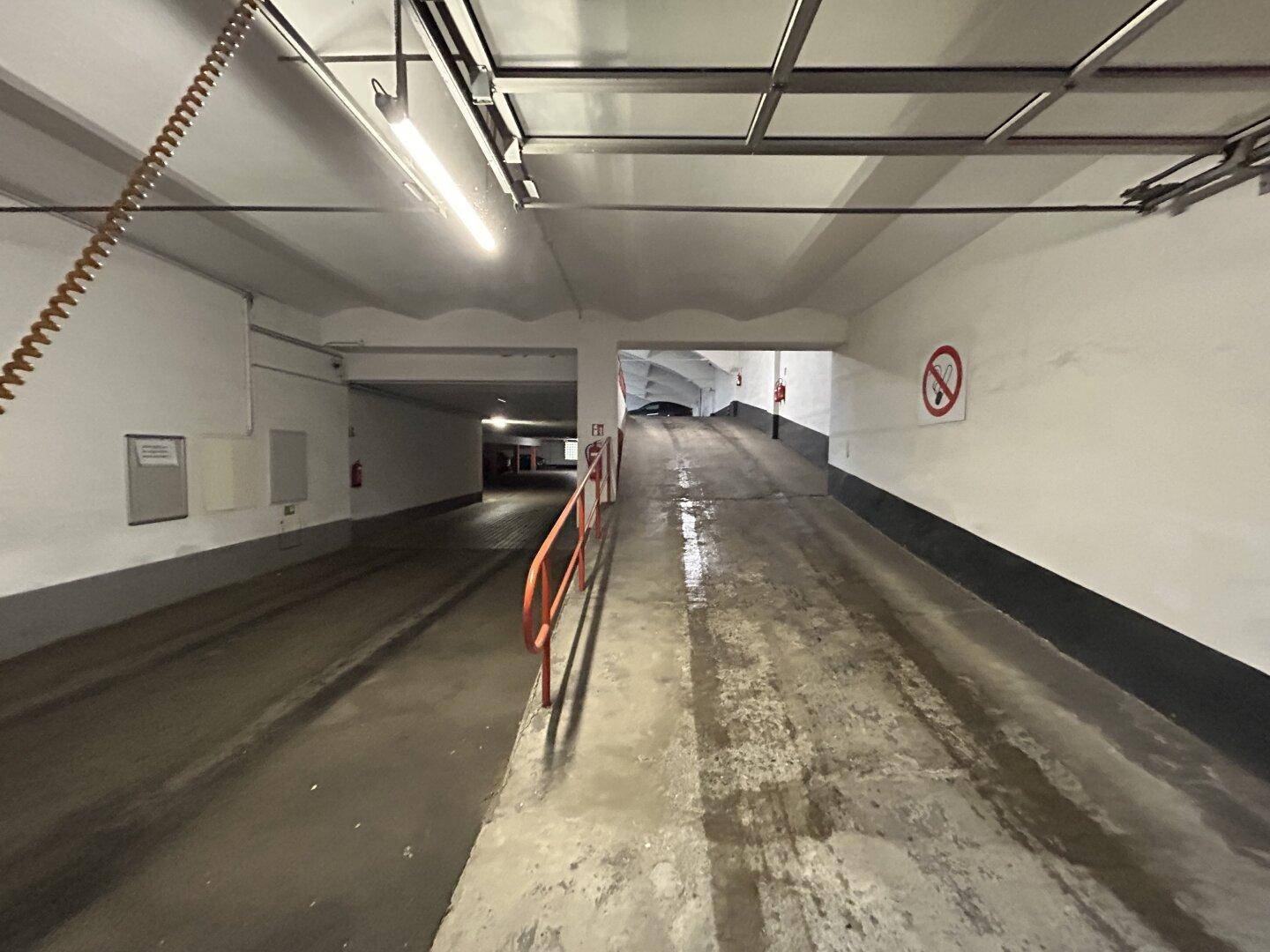 Zufahrtsrampe zu einer Tiefgarage mit Betonwänden und Beleuchtung.