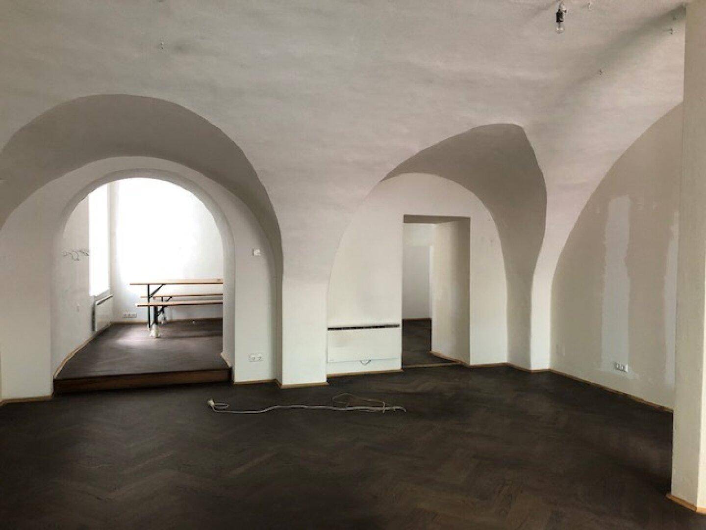 Geräumiger Innenbereich mit mehreren Gewölbebögen, die zu angrenzenden Räumen führen, und dunklem Holzboden.