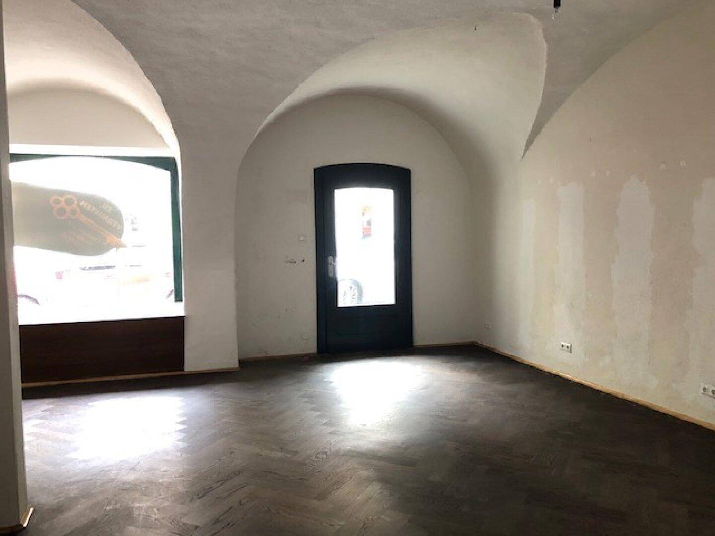 Innenraum mit beeindruckenden Gewölbedecken, dunklem Fischgrätparkett und einem großen Fensterbereich.