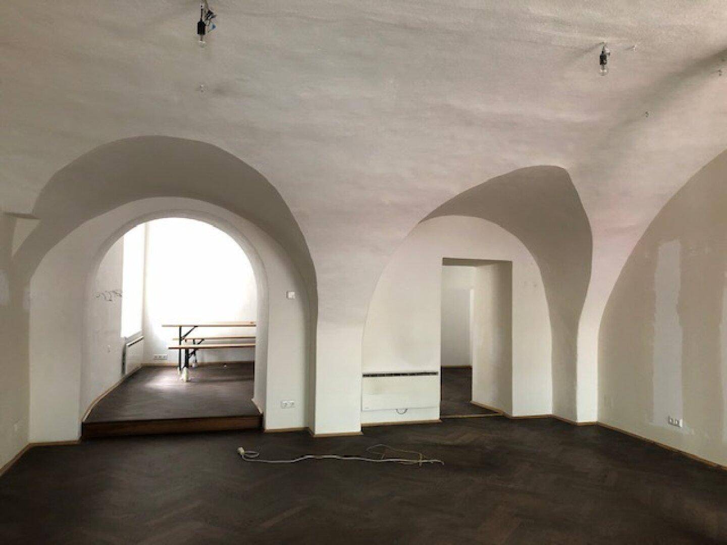 Geräumiger Innenbereich mit mehreren Gewölbebögen, die zu angrenzenden Räumen führen, und dunklem Holzboden.