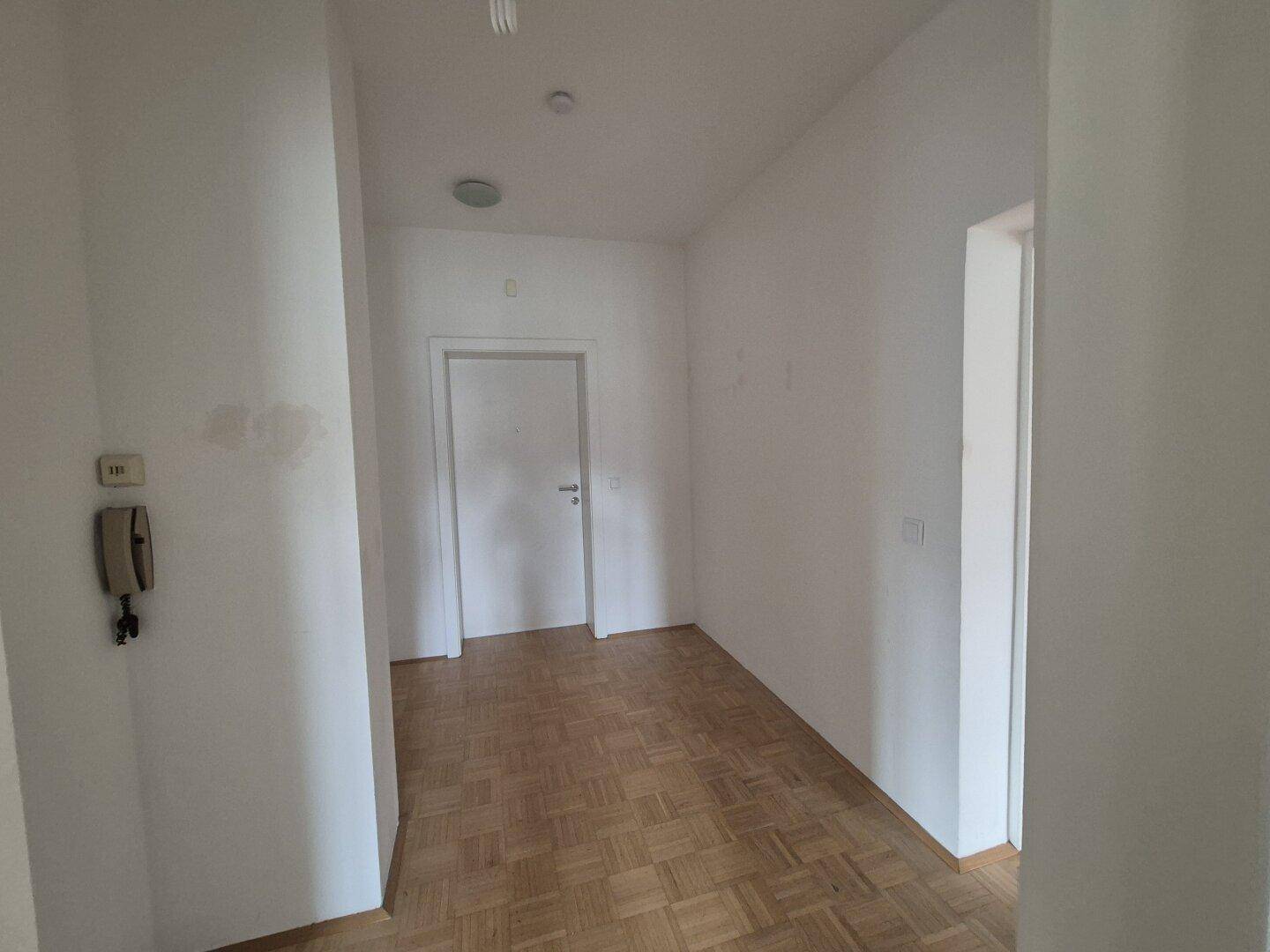 Eingangsbereich oder Flur mit Parkettboden und einer Gegensprechanlage an der Wand.