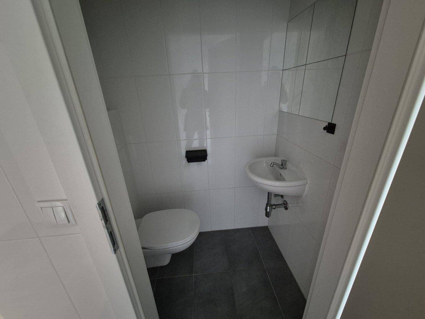 Kleines Gäste-WC mit Toilette, Waschbecken und weißen Wandfliesen.