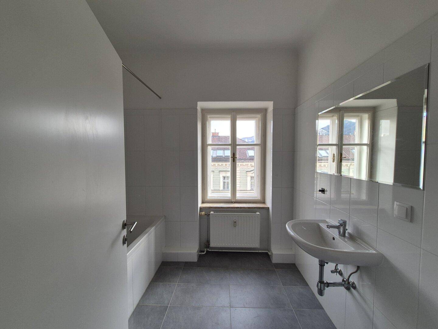 Helles Badezimmer mit Badewanne, Waschbecken, Spiegel und einem Fenster.