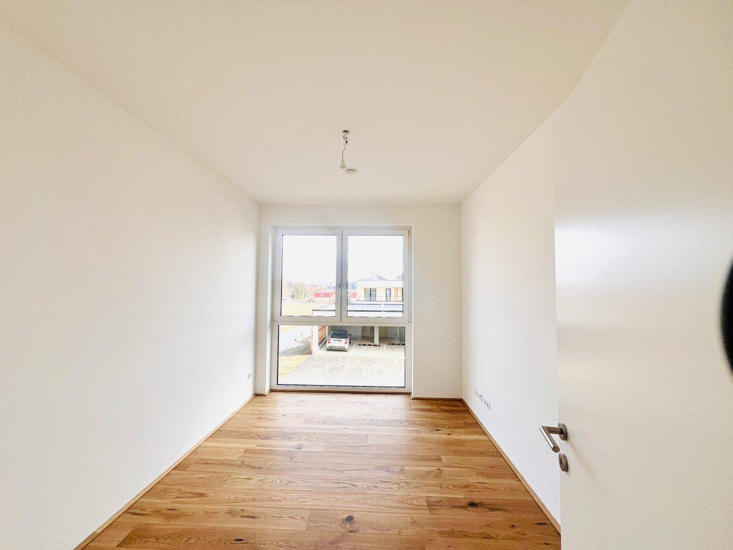 Helles Schlafzimmer mit Holzboden und einem Fenster mit Blick auf den Außenbereich.