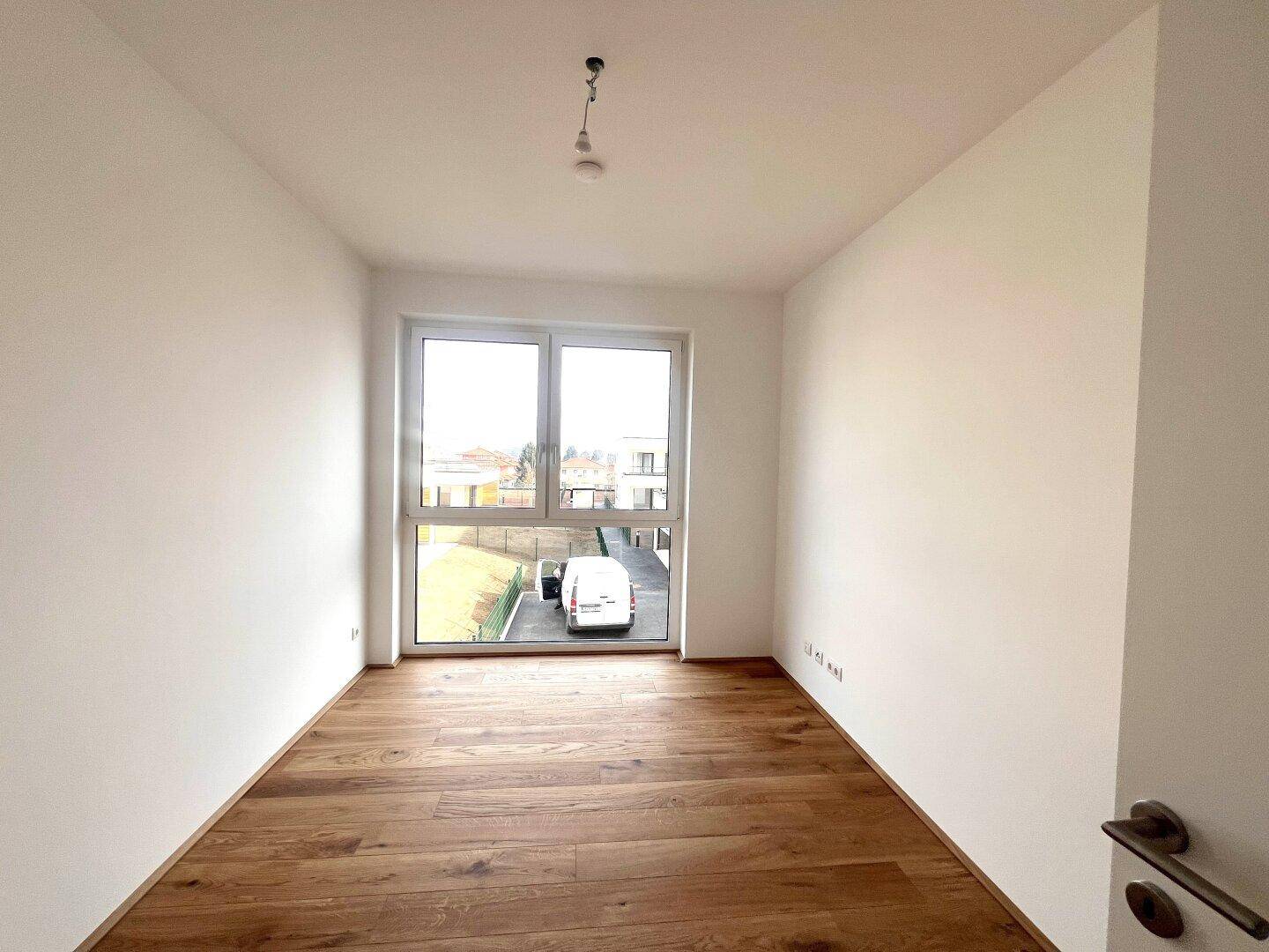 Helles Schlafzimmer mit Holzboden und großem Fenster mit Blick auf die Umgebung.