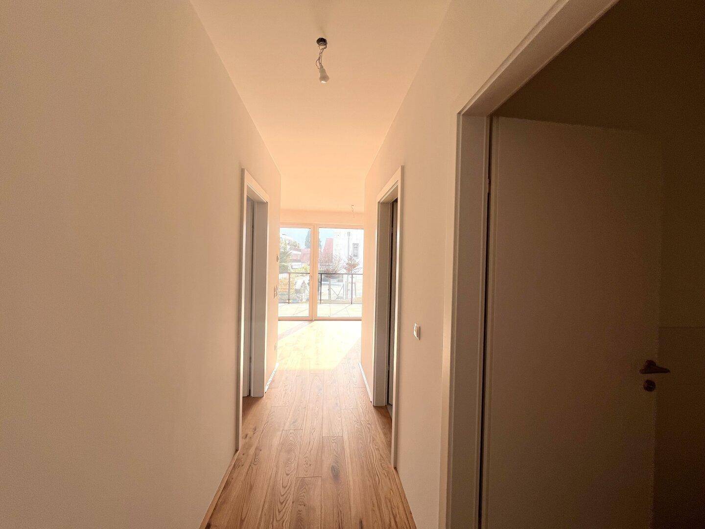 Heller Flur mit Holzboden, der zu weiteren Räumen und einem hellen Bereich führt.