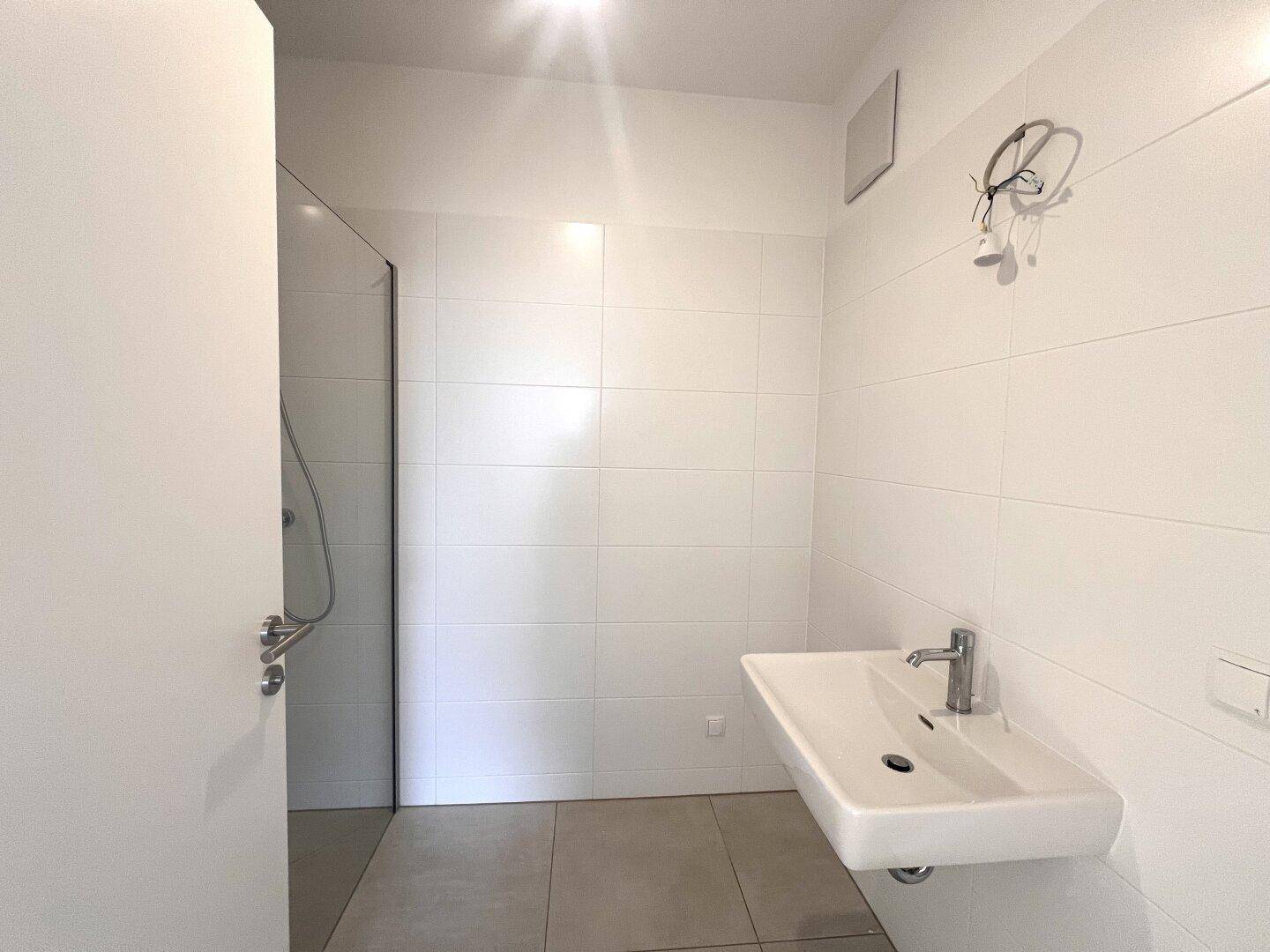 Modernes Badezimmer mit weiß gefliesten Wänden, Waschbecken und einer begehbaren Dusche.