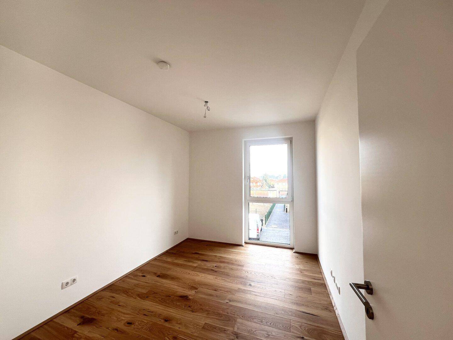 Weiteres helles Zimmer mit Holzboden und Fenster, ideal als Schlaf- oder Arbeitszimmer.