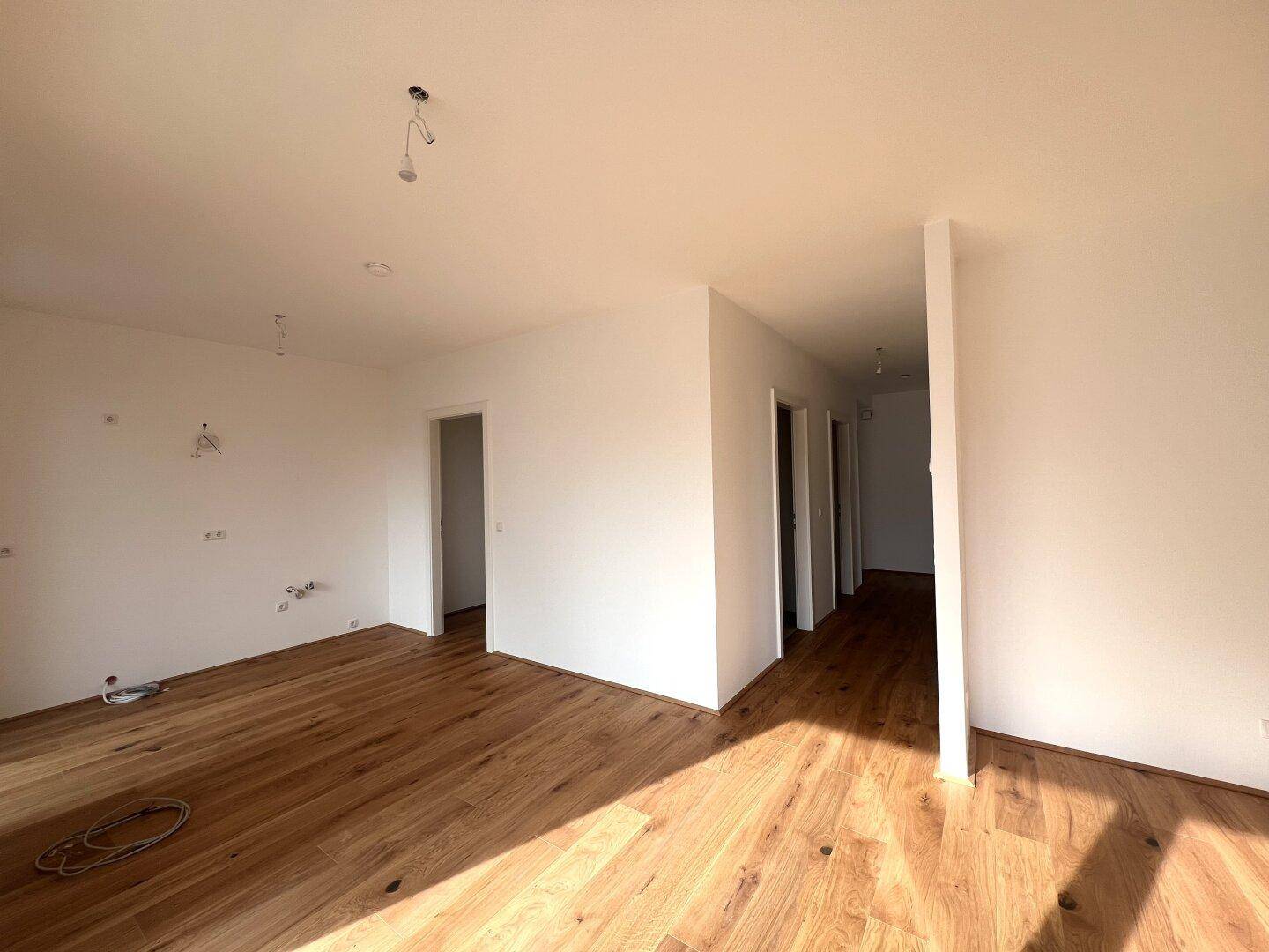 Geräumiger, heller Raum mit Holzboden und mehreren Türen, der in einen Flur führt.