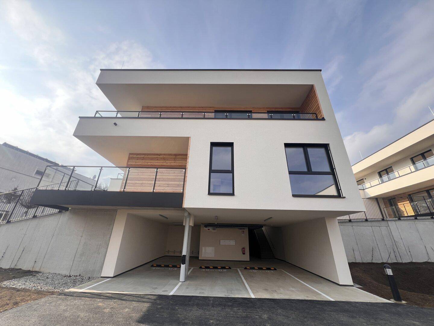 Moderne Architektur eines Neubaus mit klaren Linien, Balkonen und überdachten Parkplätzen.