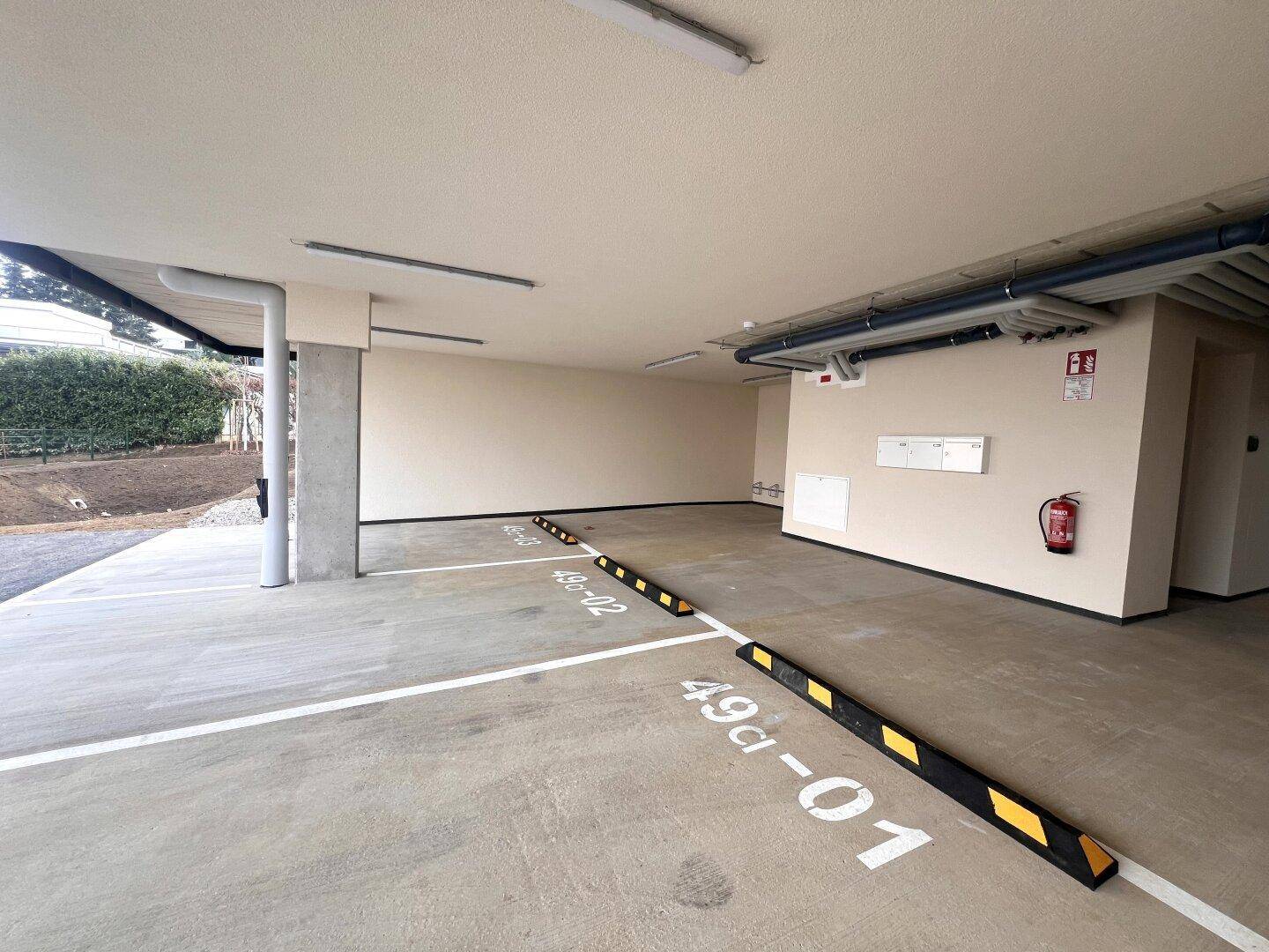 Überdachter Parkplatzbereich mit markierten Stellplätzen und direktem Zugang zum Gebäude.