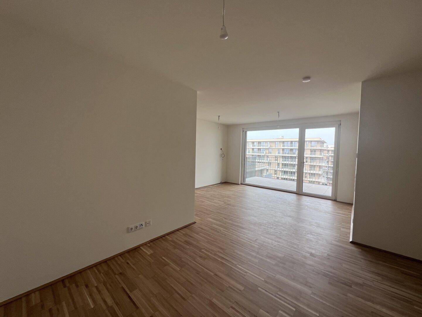 Geräumiges Wohnzimmer in einem Neubau mit hellem Parkett und weitem Blick aus den großen Fenstern.