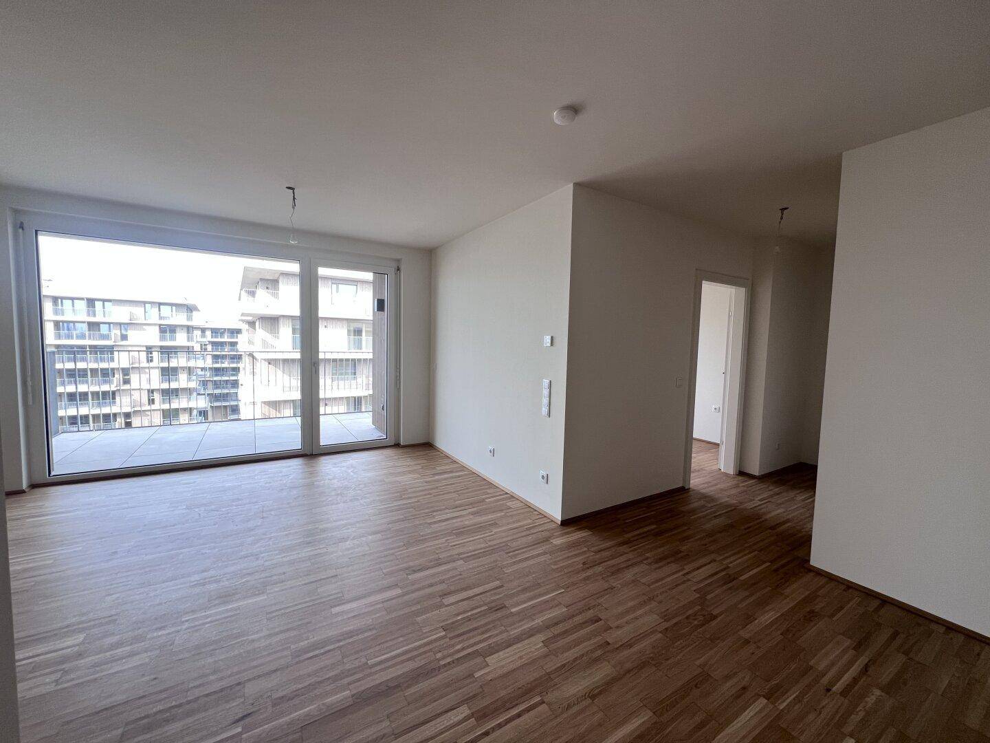 Helles Wohnzimmer mit Parkettboden, großen Fenstern und Zugang zu einem Balkon mit Stadtblick.
