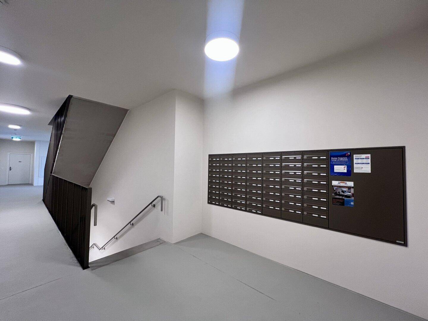 Eingangsbereich mit Briefkästen und Treppenhaus in einem modernen Wohngebäude.