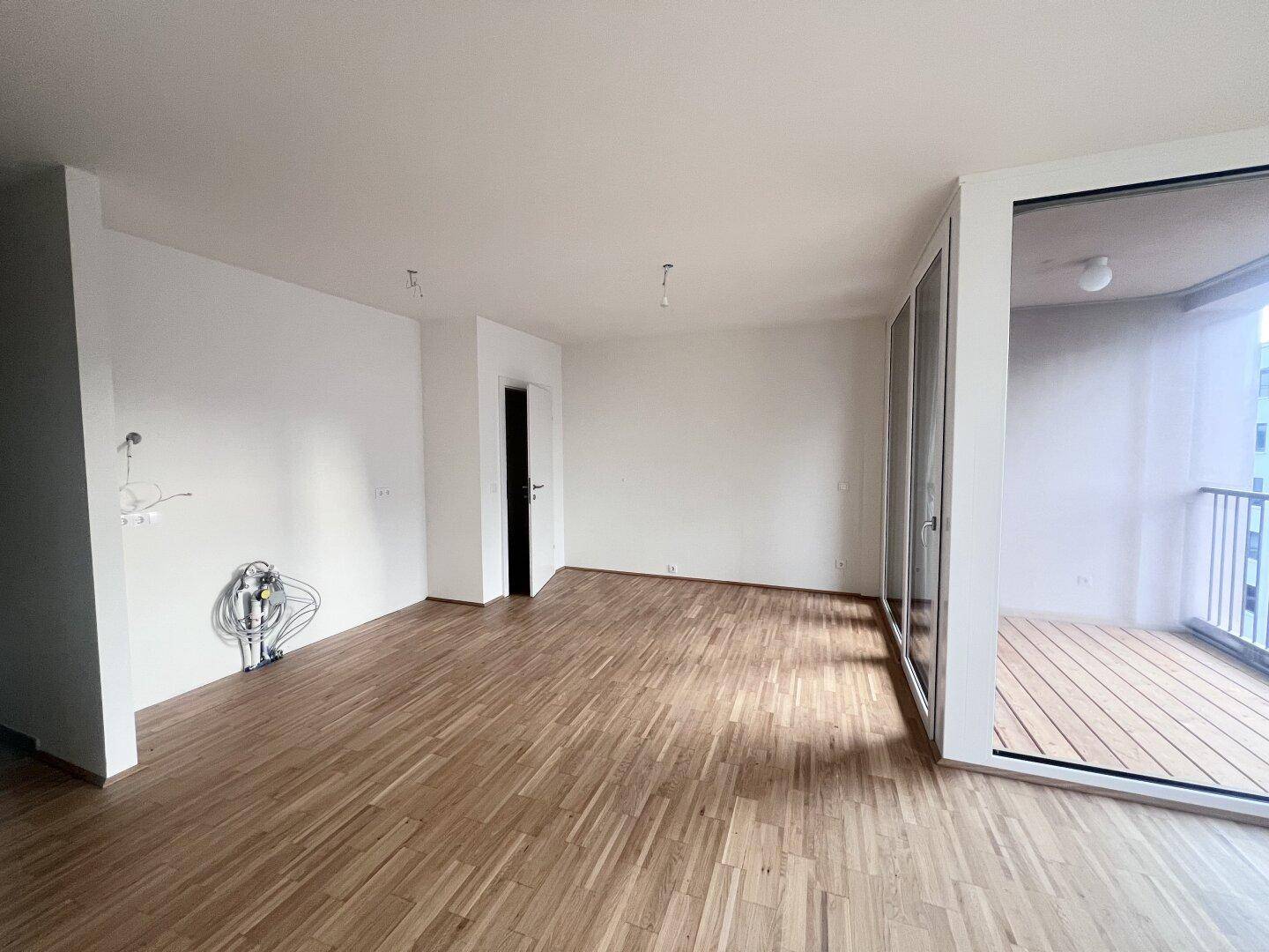 Heller, leerer Wohnraum mit Parkettboden und direktem Zugang zu einem Balkon.