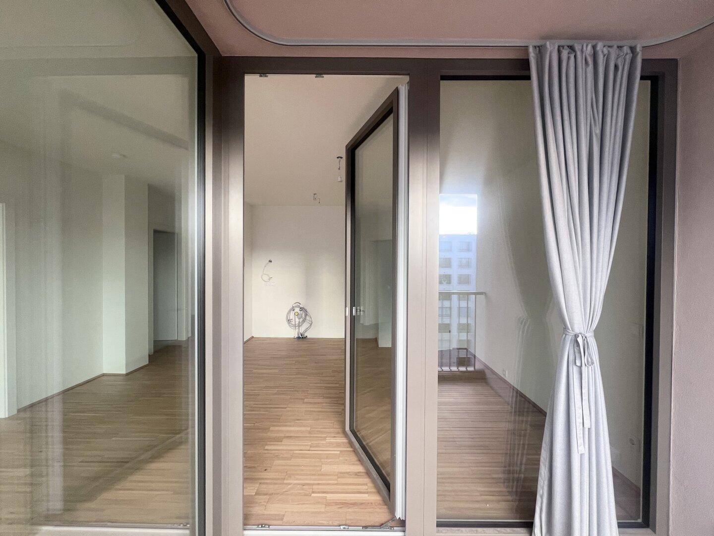 Balkonzugang mit Vorhang und Blick in den hellen, leeren Wohnbereich der Wohnung.