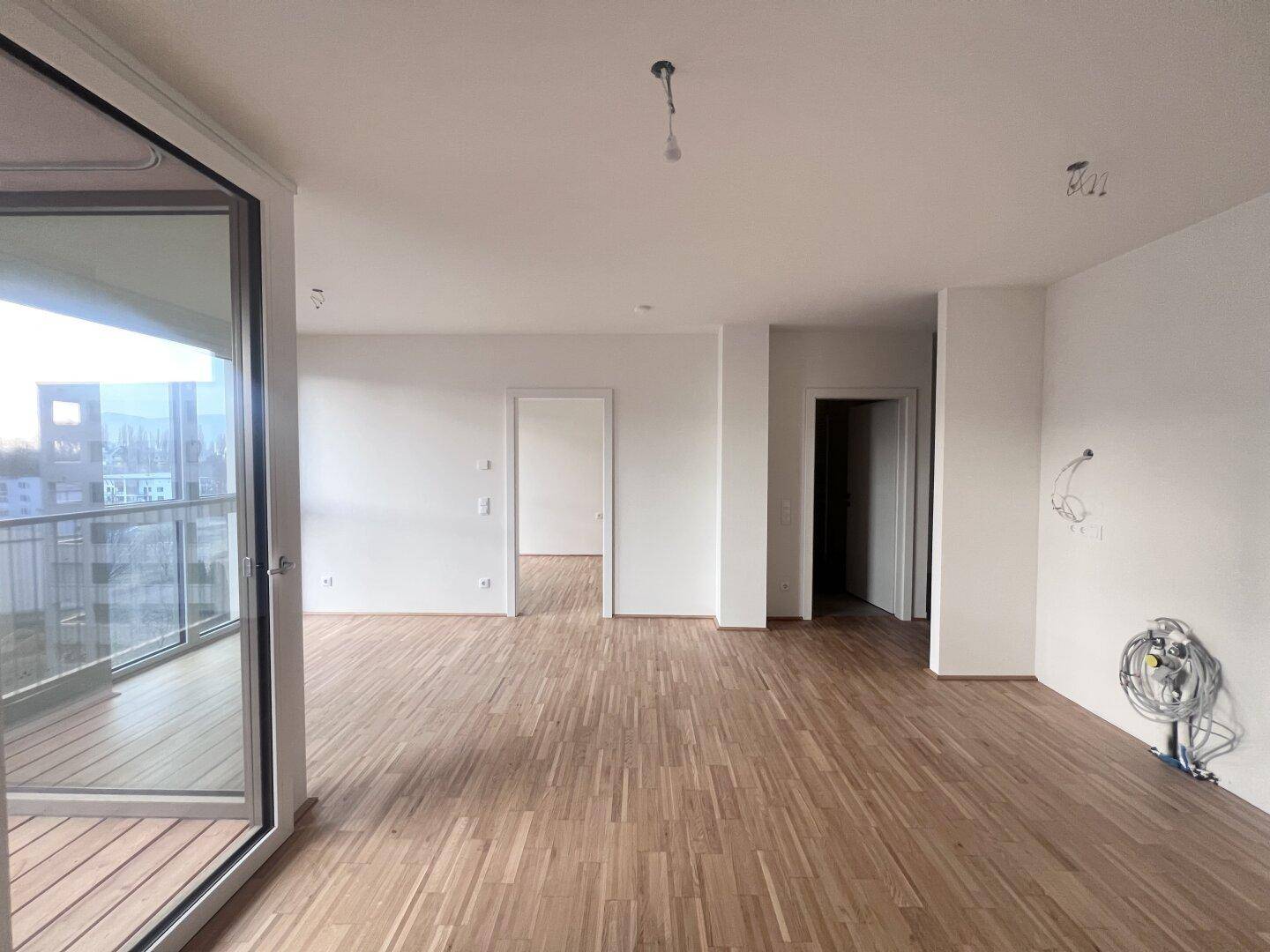 Geräumiger, leerer Wohnbereich mit Parkettboden und direktem Zugang zum Balkon.