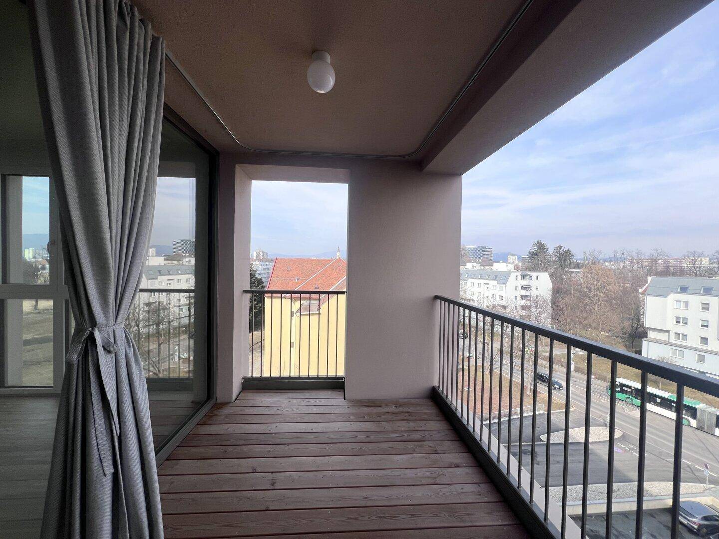 Geräumiger Balkon mit Holzboden und weitem Blick über die städtische Umgebung.
