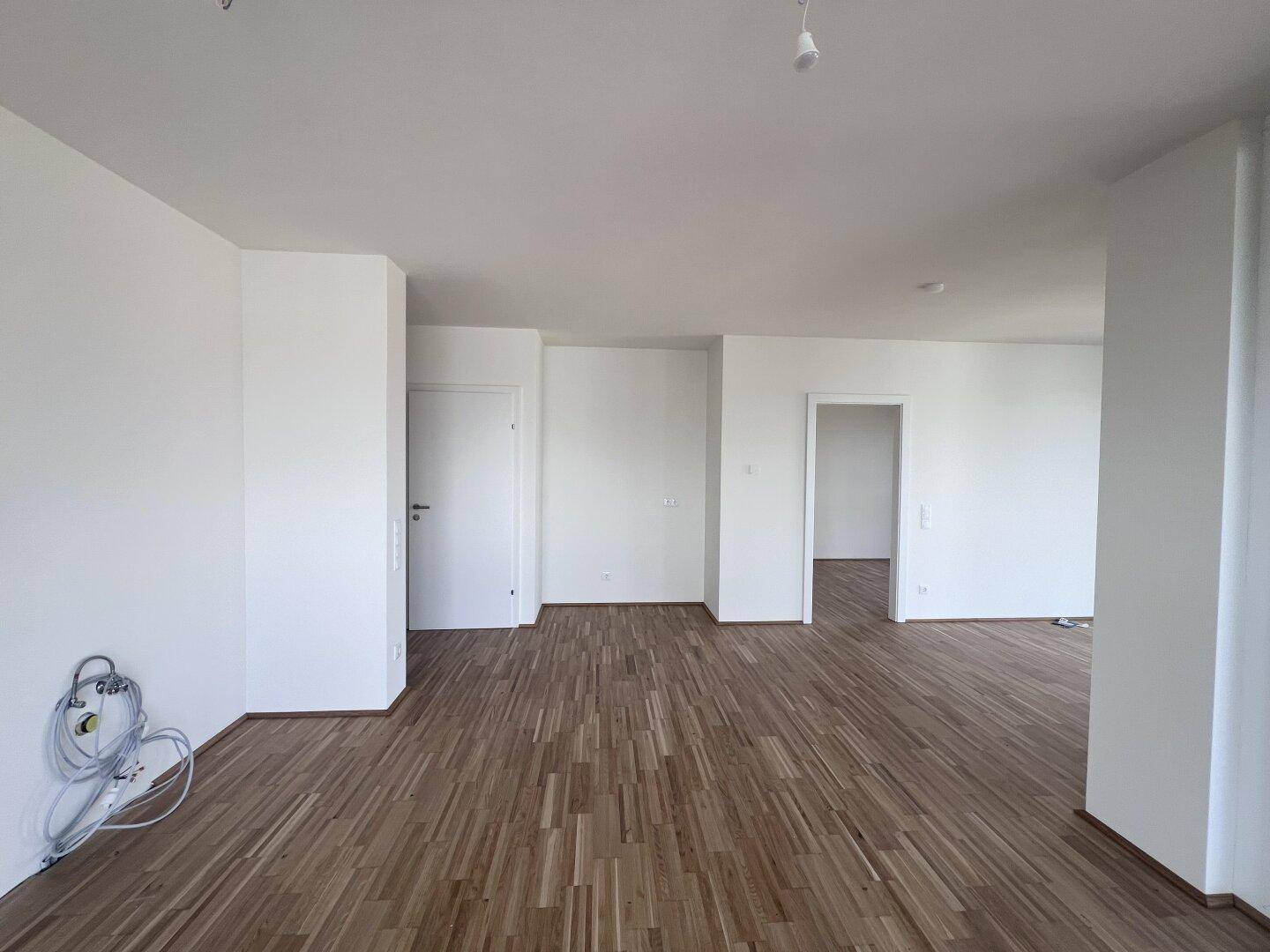 Leerer Raum mit Holzboden und mehreren Türen, der vielseitig nutzbar ist.