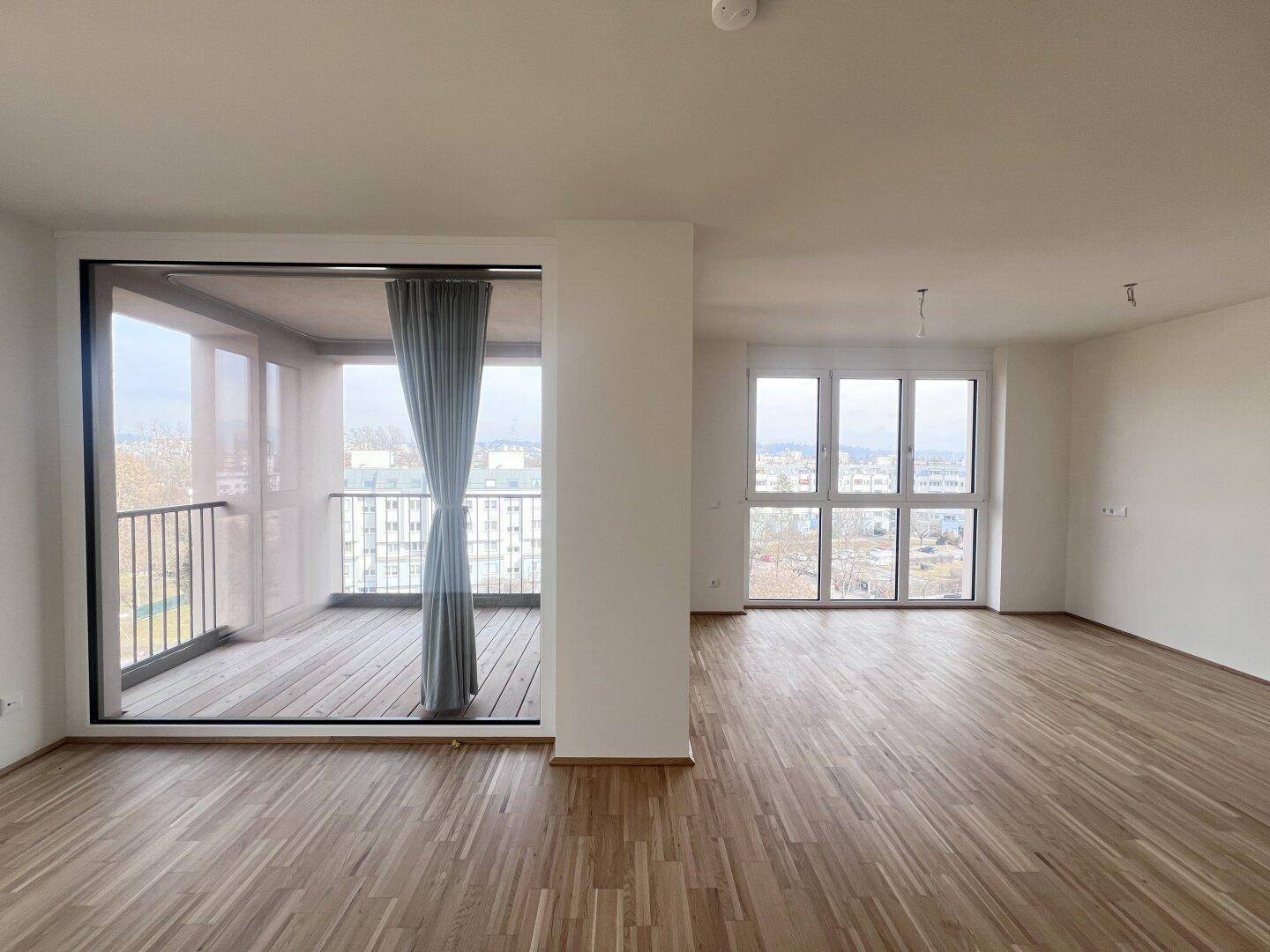 Lichtdurchflutetes Wohnzimmer mit breiter Glasfront zum Balkon und Stadtblick.