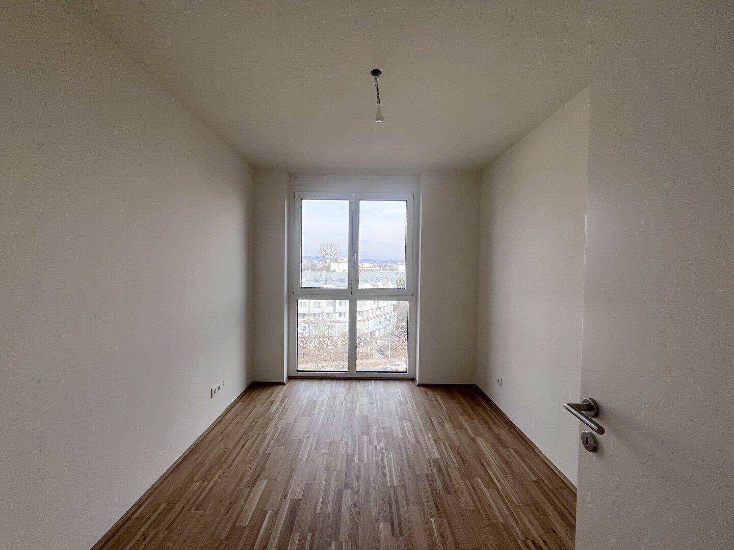 Helles Schlafzimmer mit Parkettboden und Fenster mit weitem Blick über die Stadt.