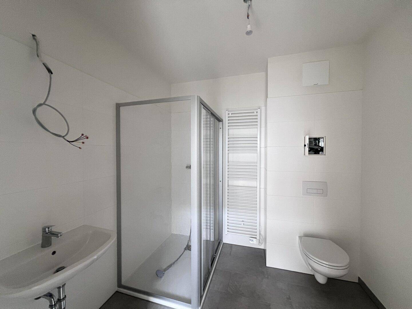 Modernes Badezimmer mit Dusche, wandhängendem WC und Heizkörper, in hellen Fliesen gehalten.