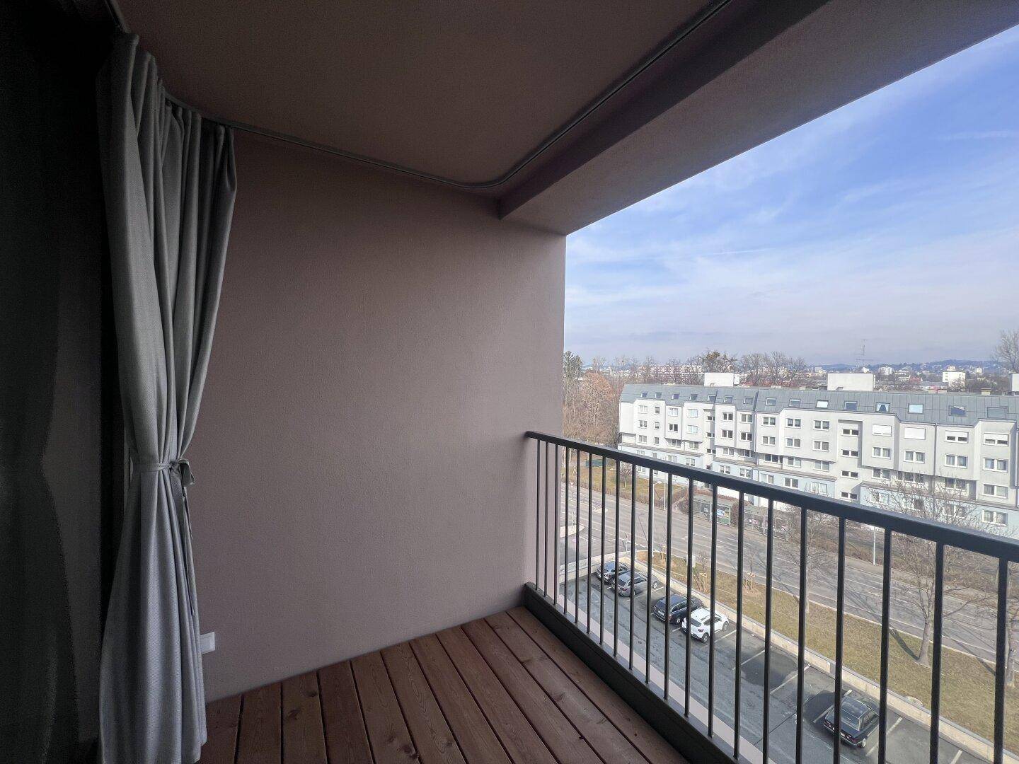 Balkon mit Holzboden und Metallgeländer, bietet einen weiten Blick auf die Umgebung und Gebäude.