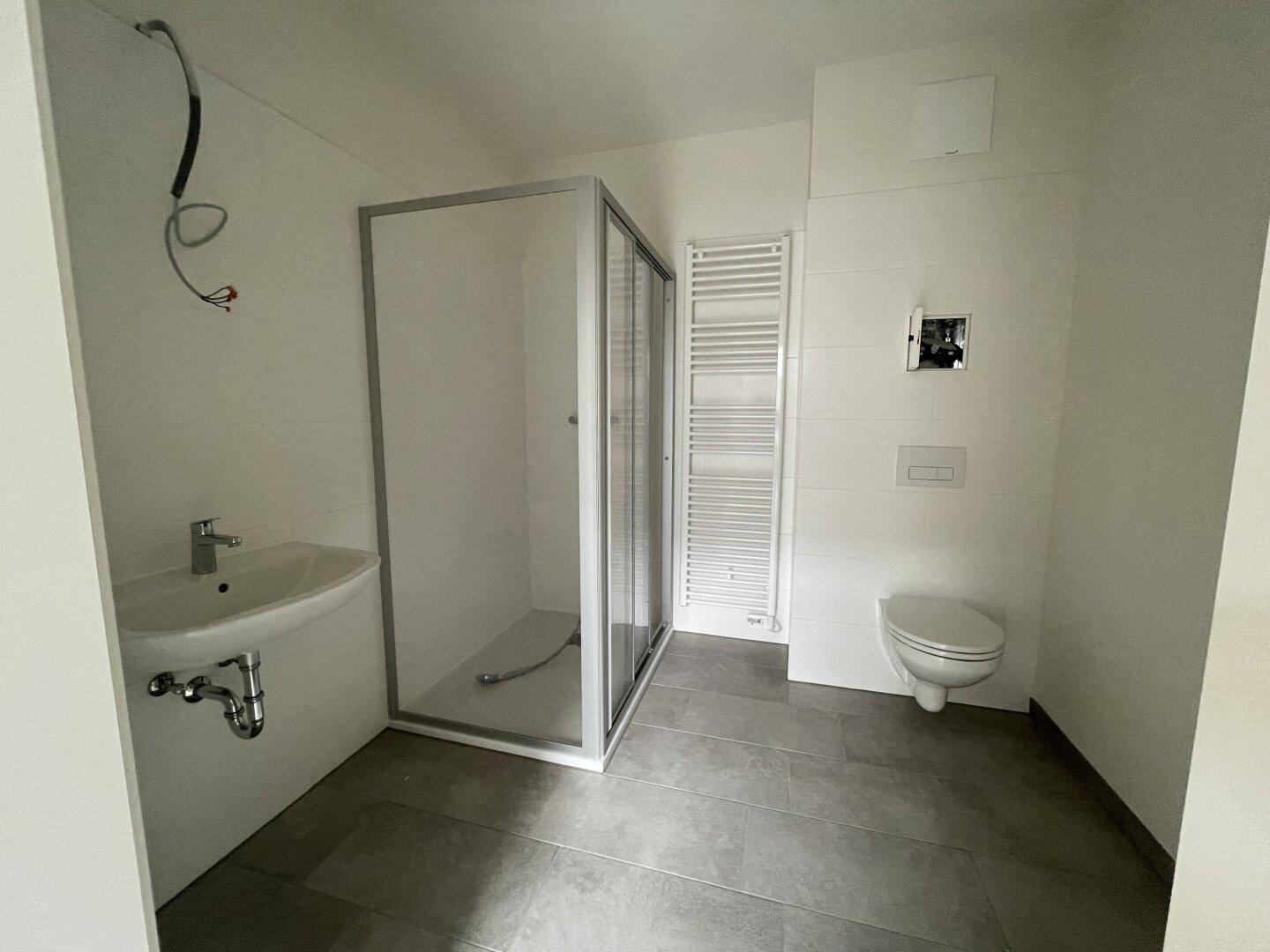Modernes Badezimmer mit Dusche, Wand-WC, Waschbecken und Handtuchheizkörper.
