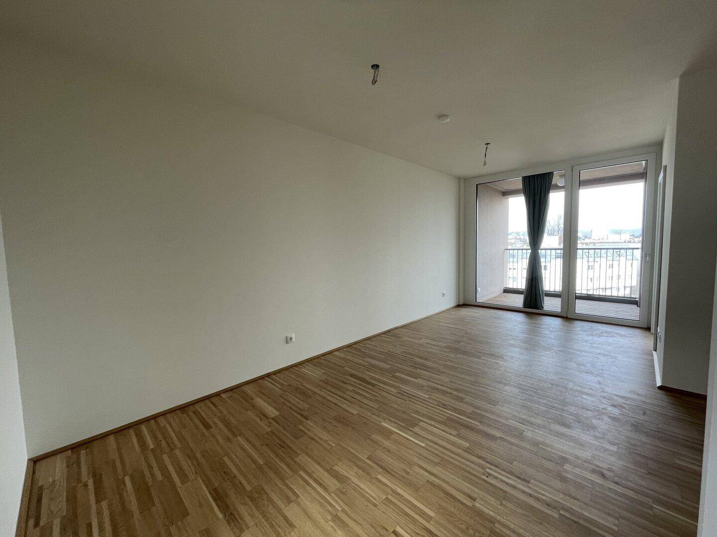 Großzügiger Wohnraum mit Parkettboden und direktem Zugang zum Balkon.