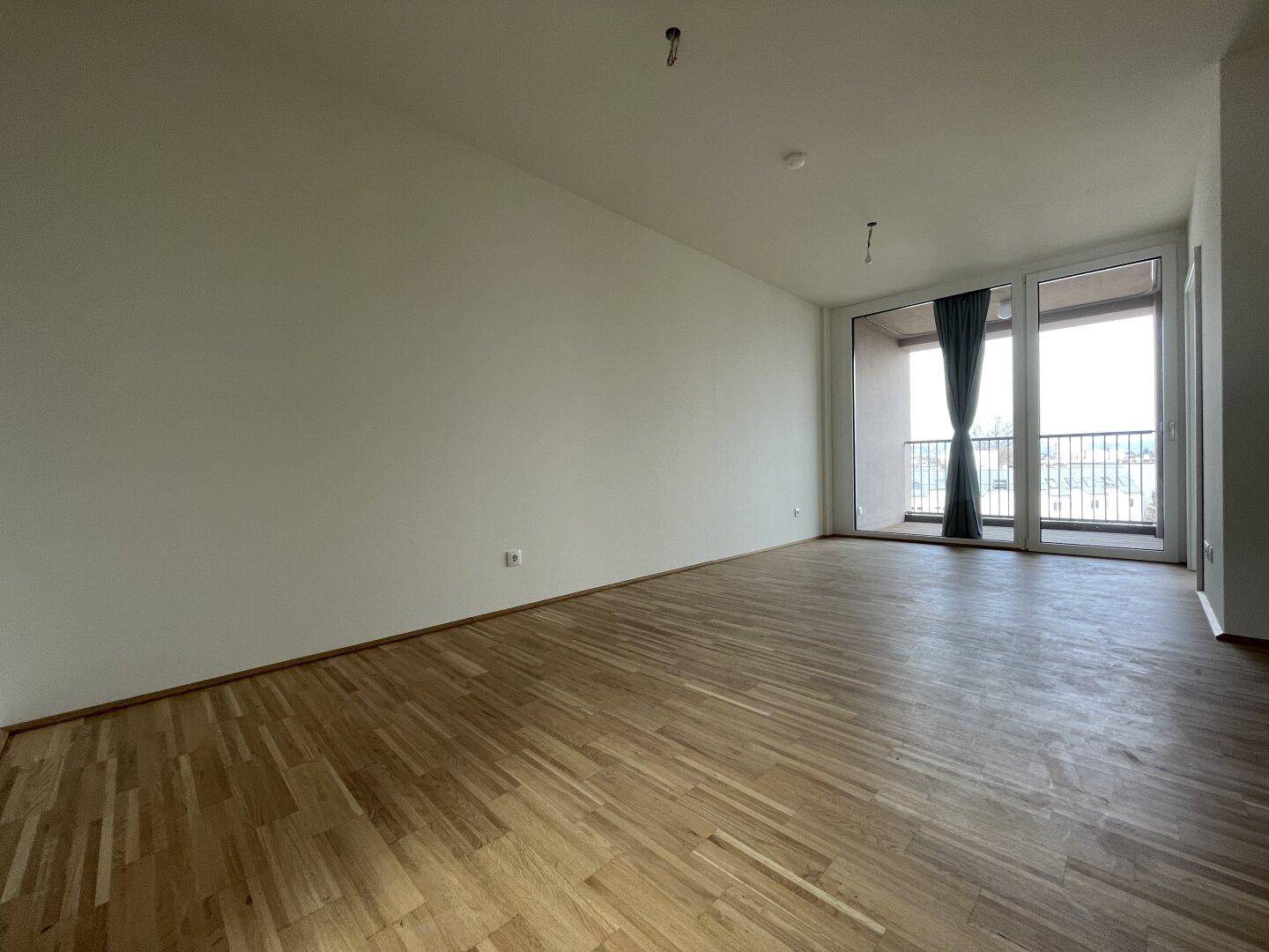 Heller Wohnbereich mit Parkettboden und großen Fenstern zum Balkon.