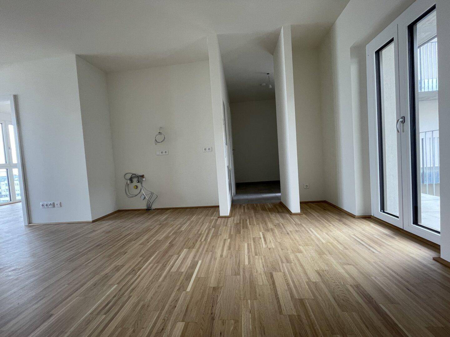 Offener Bereich mit Parkettboden und Anschlüssen für eine zukünftige Küche.
