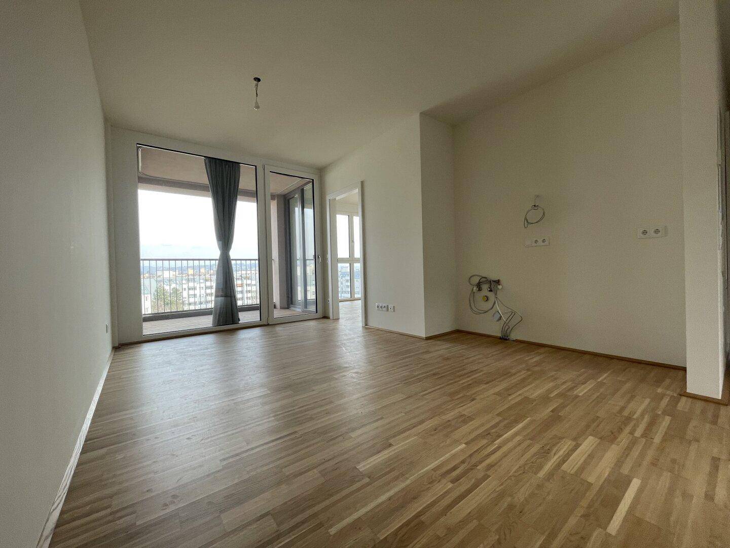 Heller Wohnbereich mit Parkettboden und Zugang zu einem überdachten Balkon.