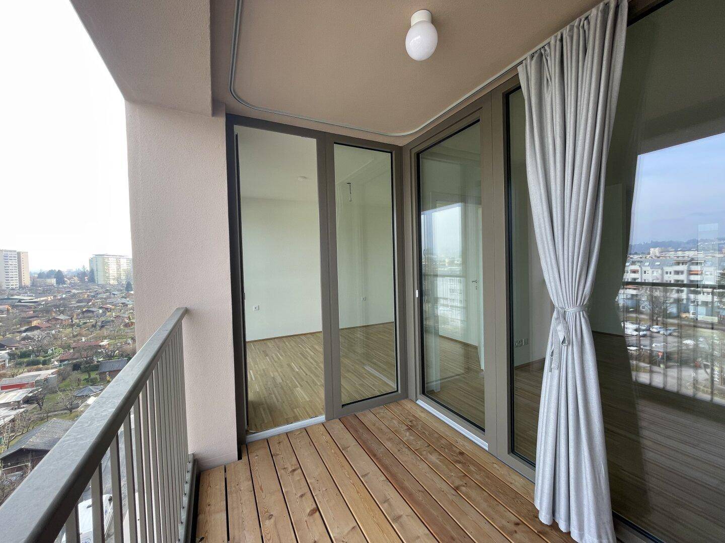 Geräumiger Balkon mit Holzboden und weitem Blick über die städtische Umgebung.