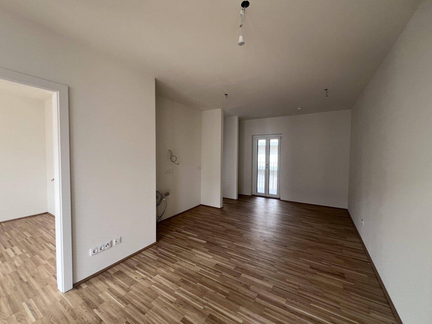 Heller, leerer Wohnraum mit Parkettboden und Zugang zu einem Balkon, bereit für die Einrichtung.