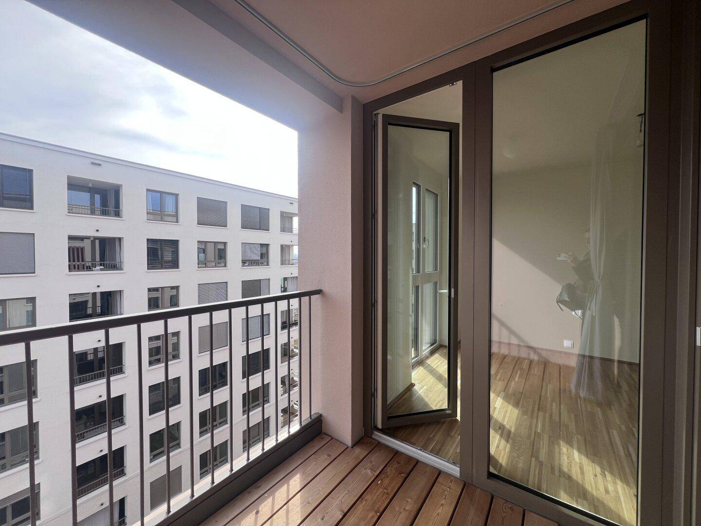 Balkon mit Holzboden und Blick auf die umliegenden Gebäude und den Innenhof, bietet eine ruhige Aussicht.
