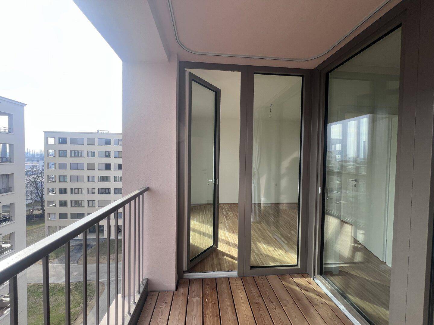 Geräumiger Balkon mit Holzboden und Blick auf die Stadt sowie andere Wohngebäude in der Umgebung.