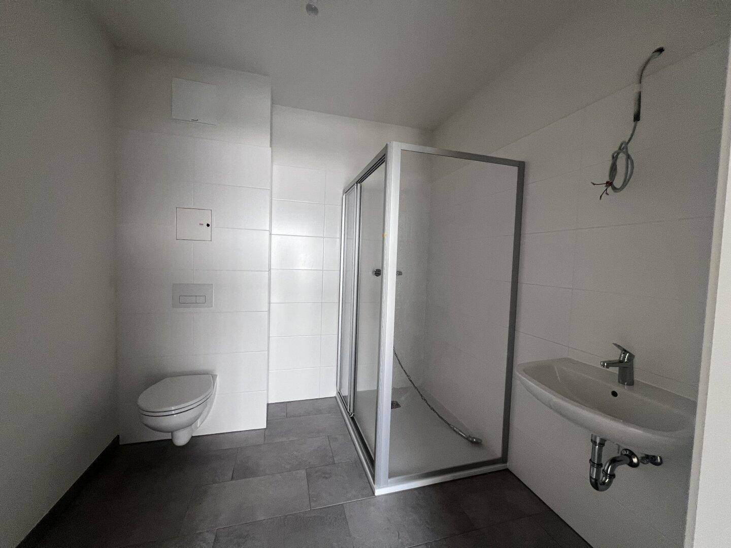 Modernes Badezimmer mit Duschkabine, Wand-WC und Waschbecken, ausgestattet mit Fliesenboden.