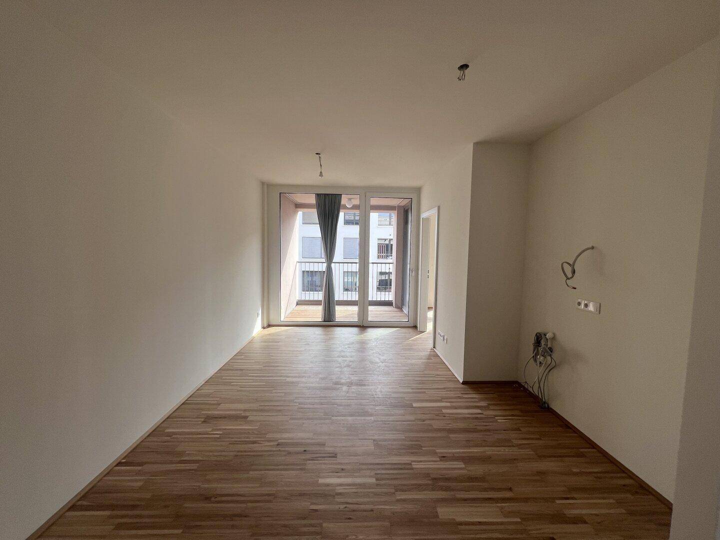 Geräumiger, heller Wohnraum mit Parkettboden und direktem Zugang zum Balkon, bietet viel Platz.
