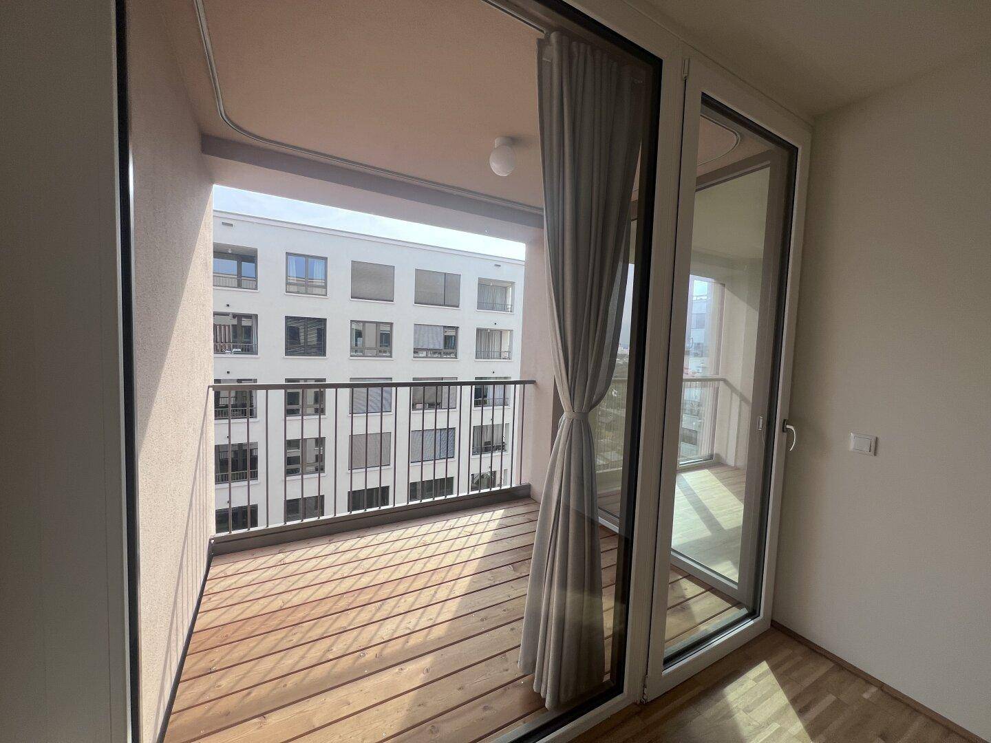 Balkon mit Holzboden und Vorhängen, bietet einen Blick auf das gegenüberliegende Gebäude.