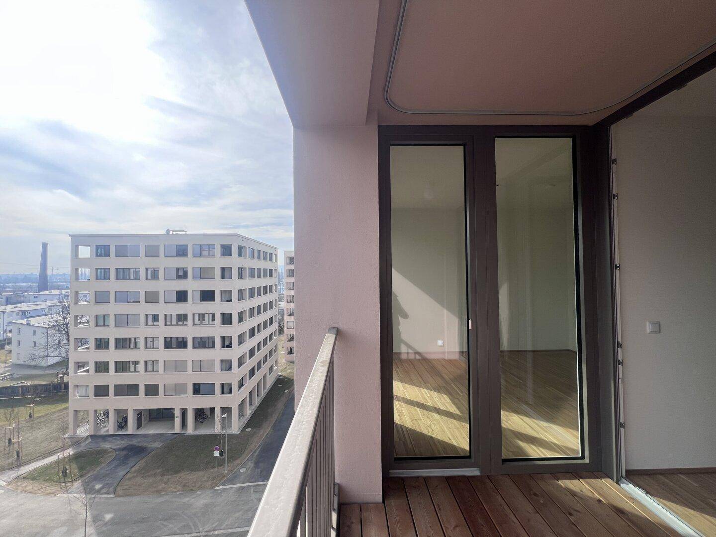 Balkon mit Holzboden und weitem Blick auf die Stadt und weitere moderne Gebäude.