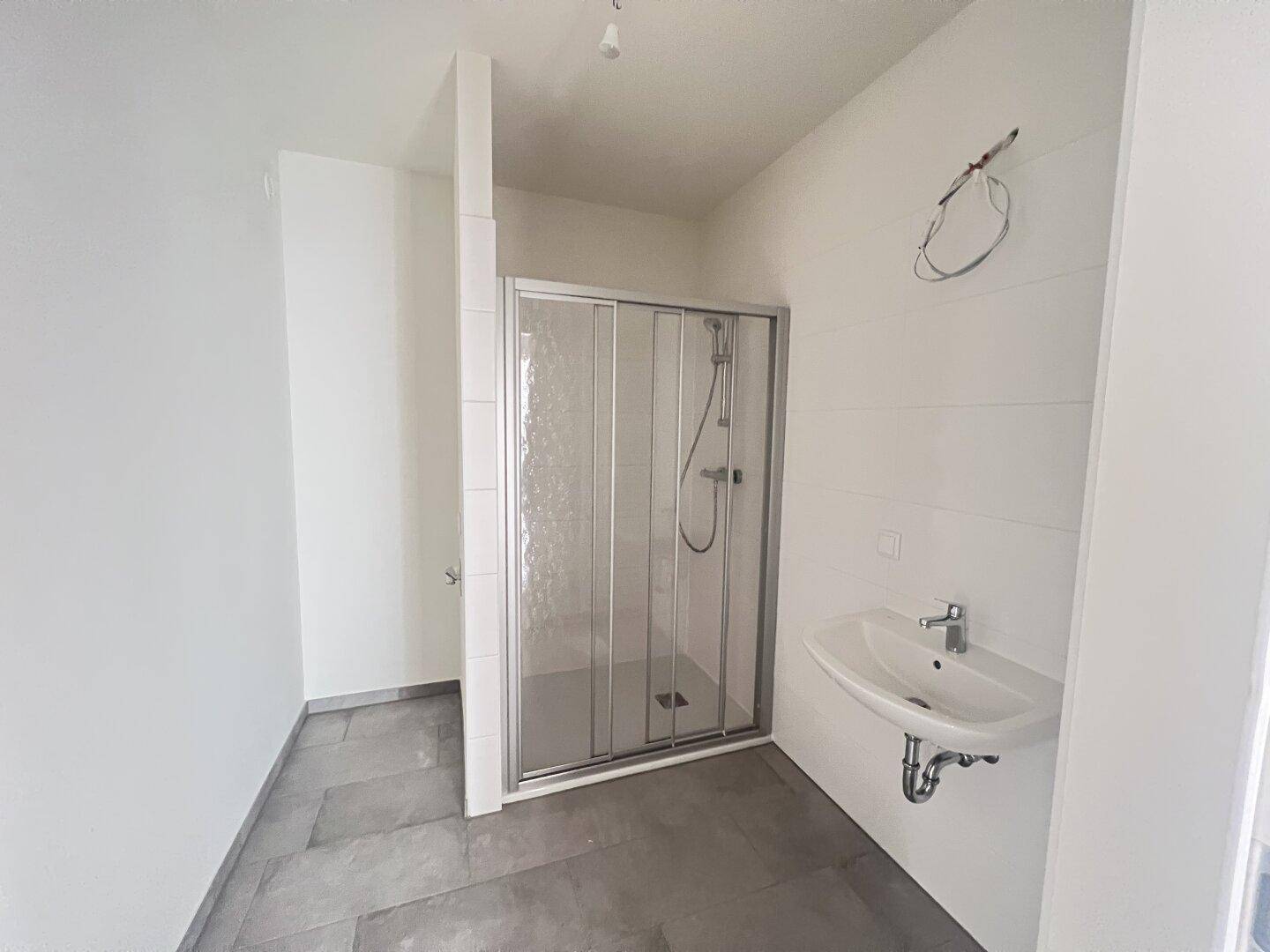 Modernes Badezimmer mit Duschkabine, Waschbecken und grauen Fliesen am Boden.