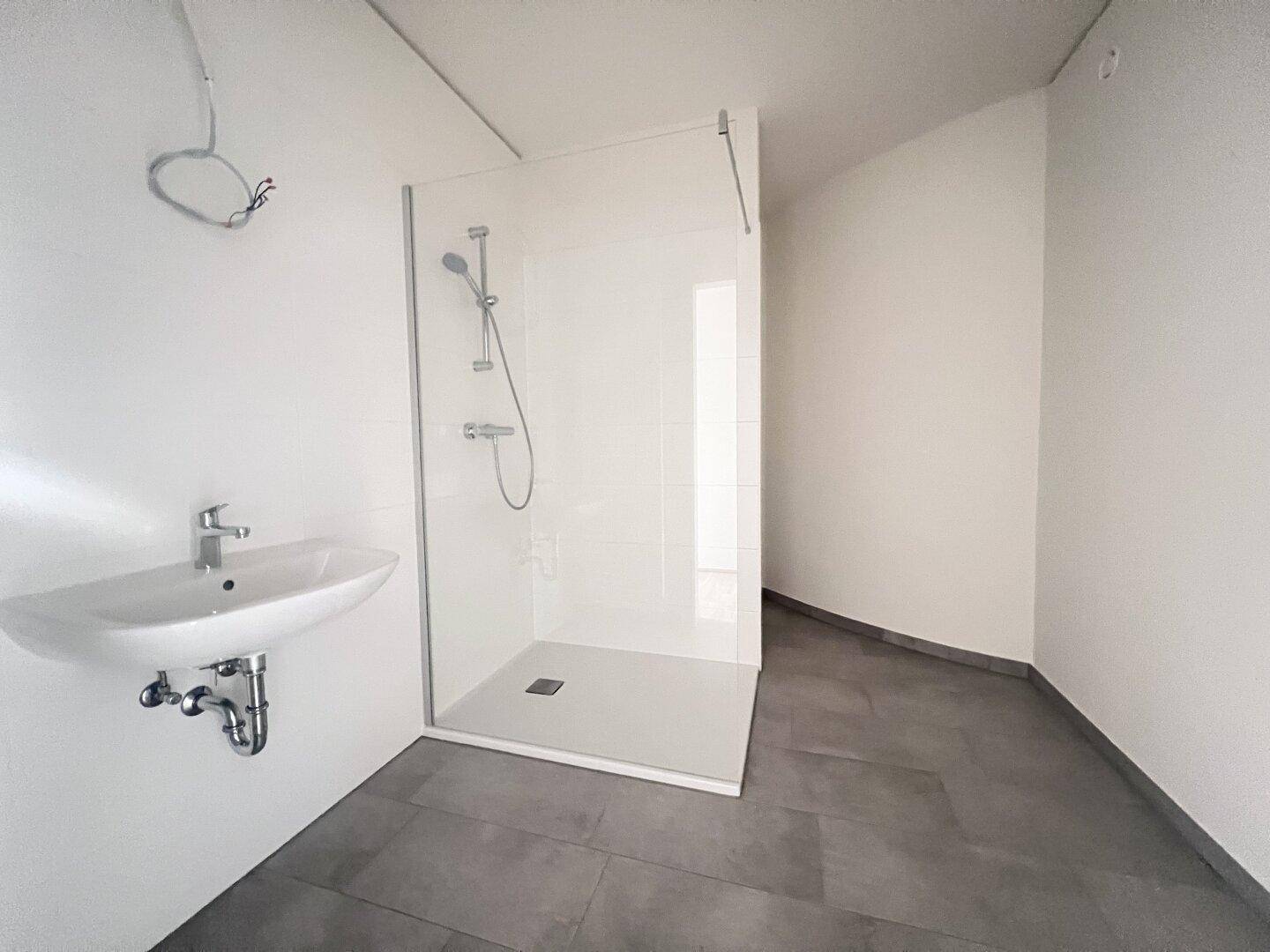 Modernes Badezimmer mit ebenerdiger Dusche und Waschbecken, in neuwertigem Zustand.